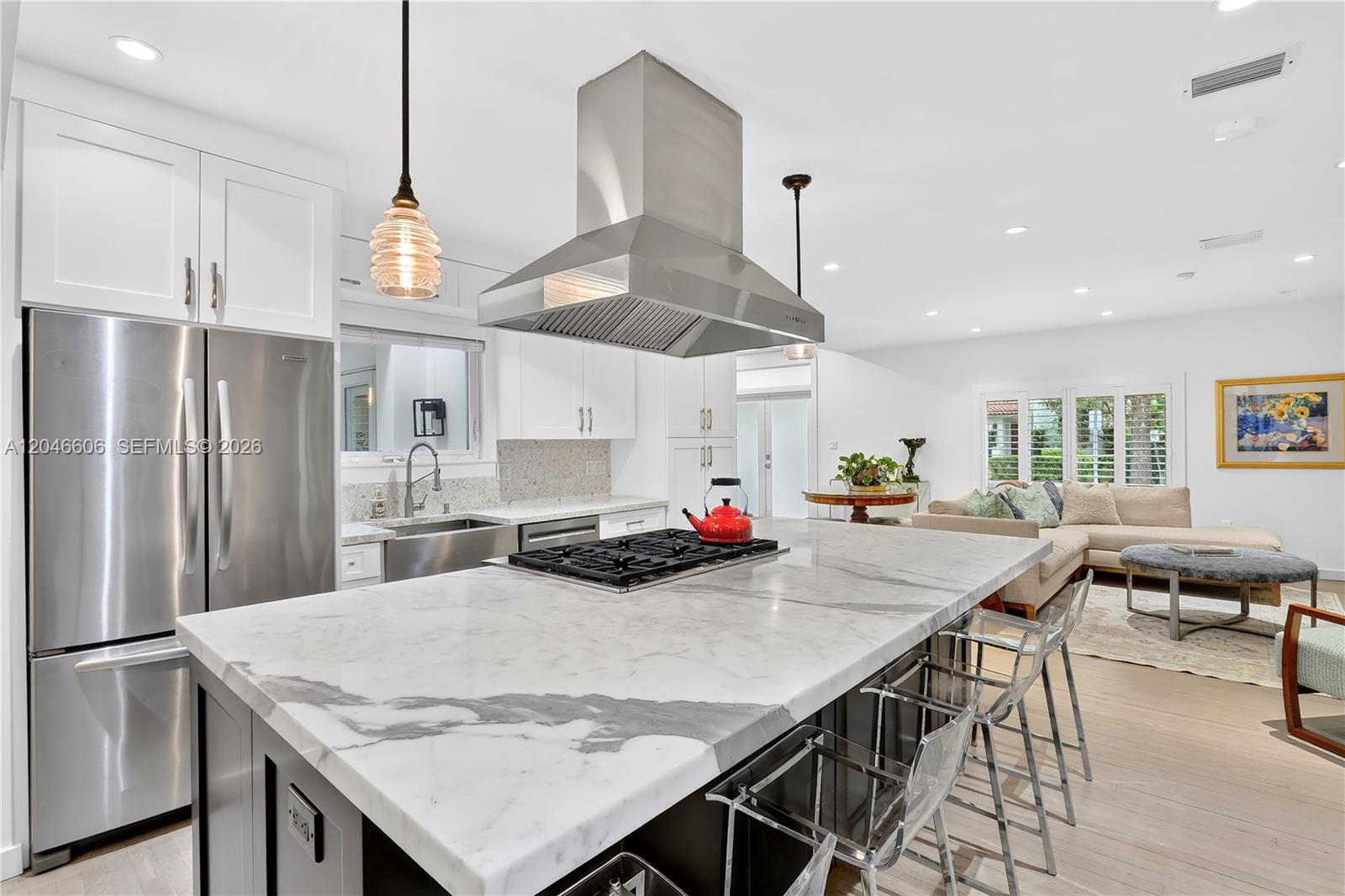 A modern kitchen features a large marble island with a gas cooktop and bar seating — 100 Sarto Ave., Coral Gables FL 33134, CORAL GABLES, FL