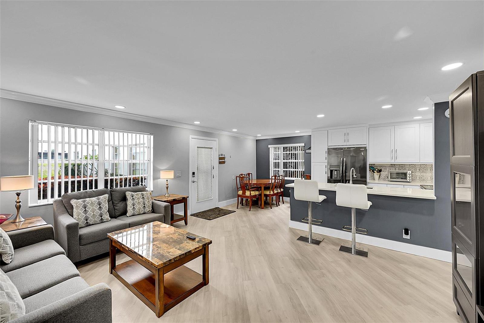 An open-concept living and dining area features gray walls, white cabinets, and light wood flooring — 964 Normandy Trail # U, Delray Beach FL 33484, DELRAY BEACH, FL