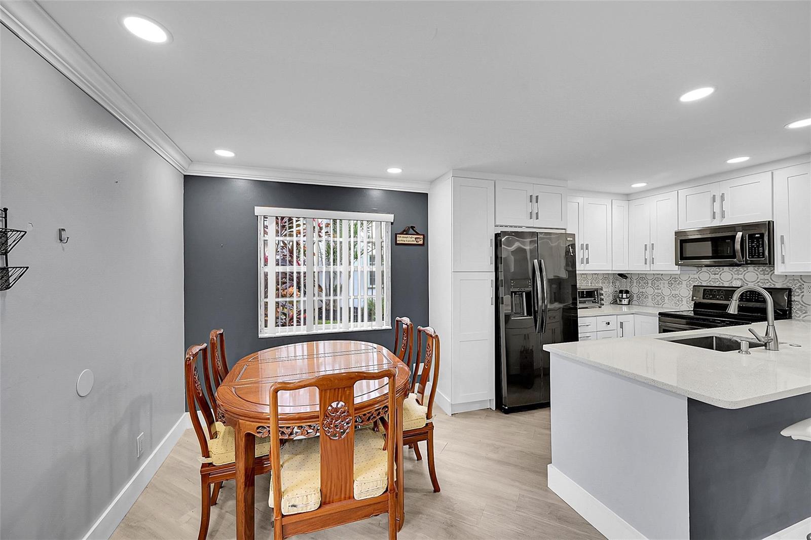 A dining area with a wooden table and chairs sits adjacent to a modern kitchen — 964 Normandy Trail # U, Delray Beach FL 33484, DELRAY BEACH, FL