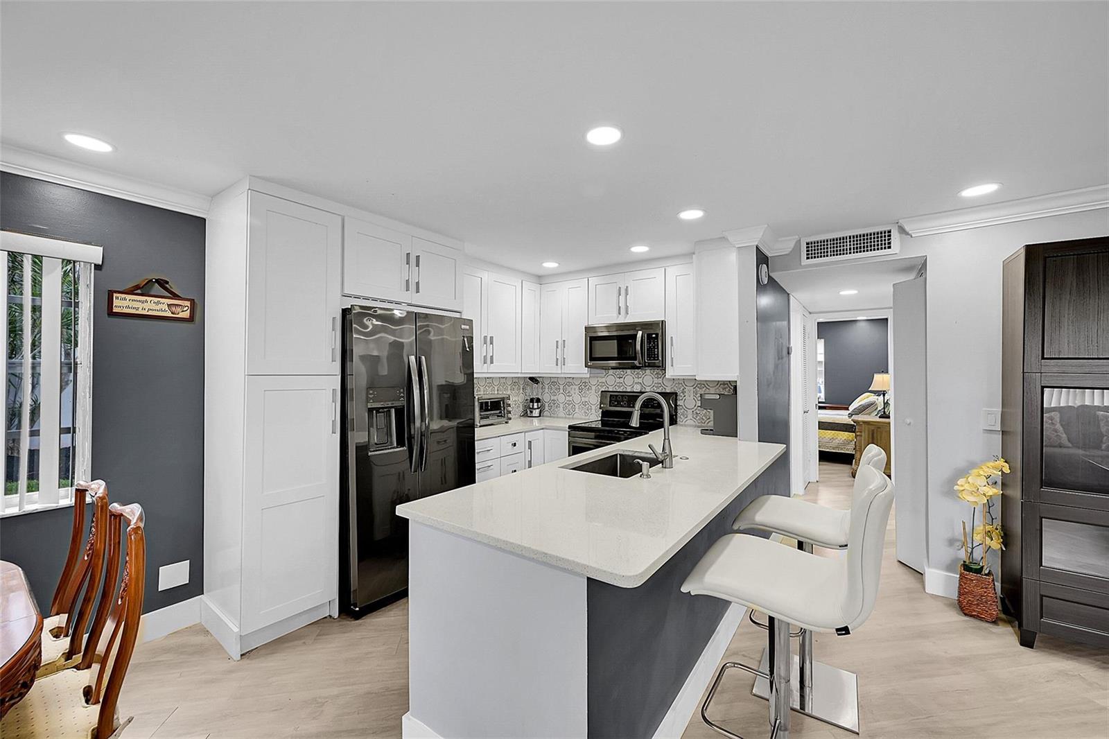A modern kitchen features white cabinetry, a quartz-topped island with bar seating, and stainless appliances — 964 Normandy Trail # U, Delray Beach FL 33484, DELRAY BEACH, FL