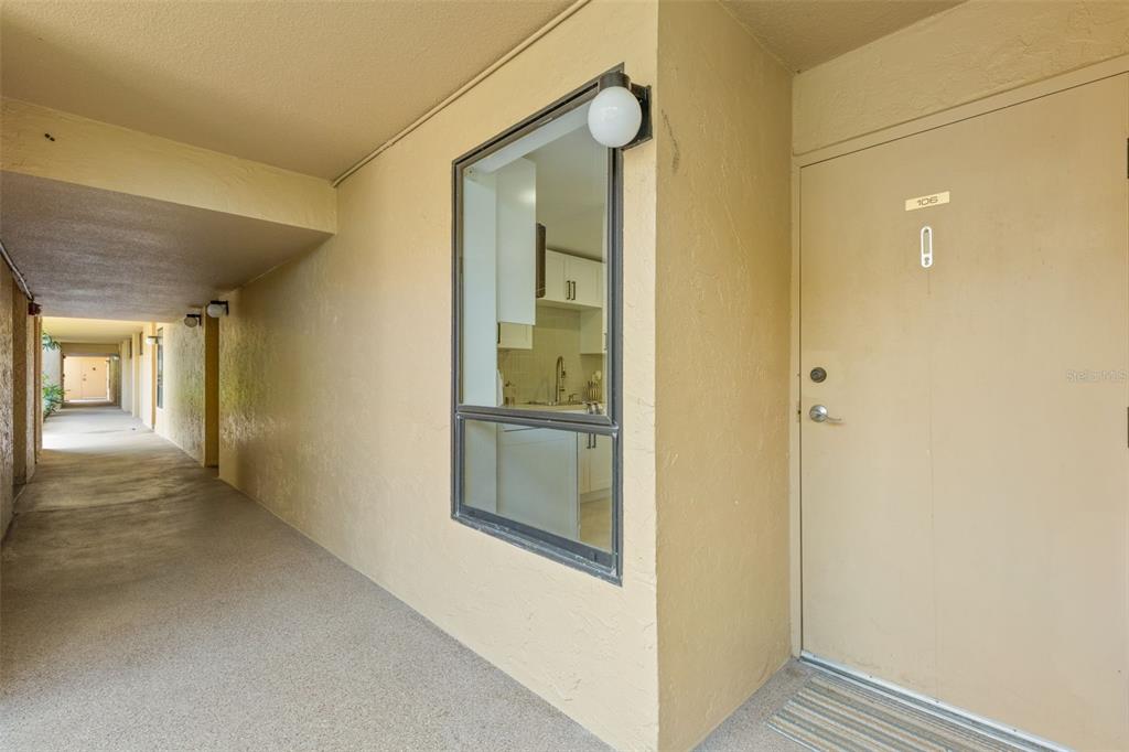 An exterior walkway leads to the entrance of unit 106, which features a kitchen window — 2614 COVE CAY DRIVE UNIT 106, CLEARWATER, FL