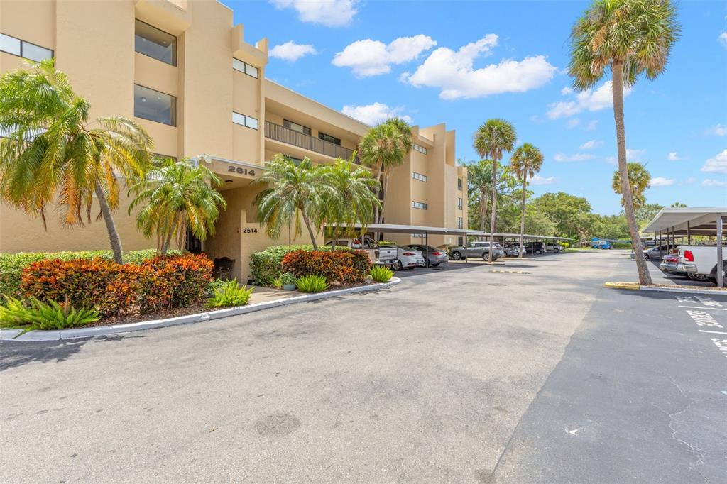 A multi-story apartment building with covered parking spaces and palm trees in the foreground — 2614 COVE CAY DRIVE UNIT 106, CLEARWATER, FL