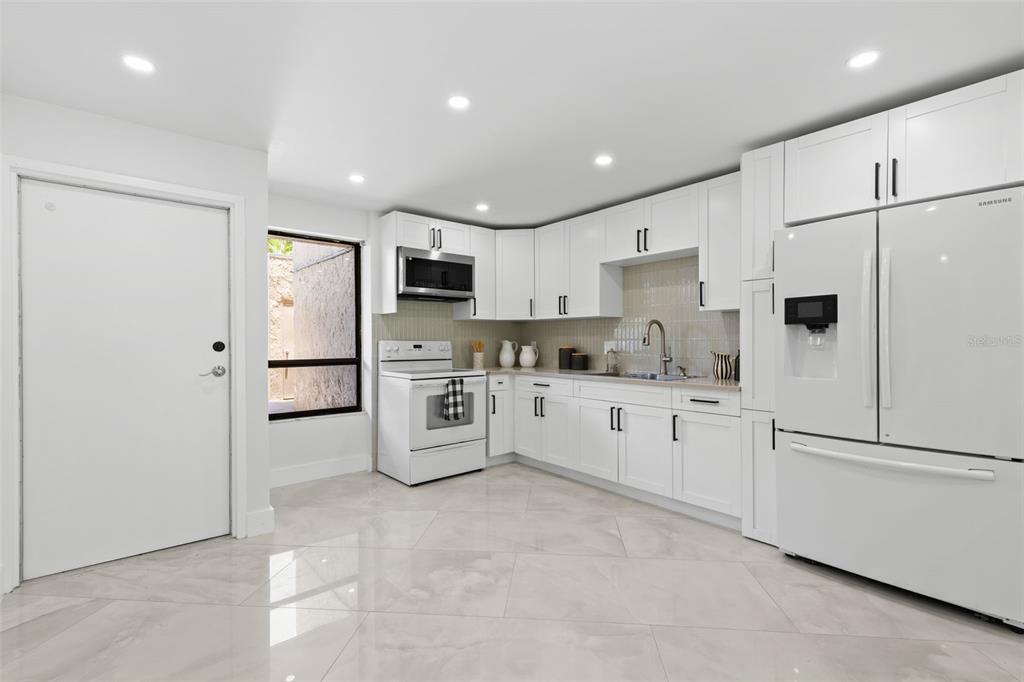 A modern kitchen features white cabinets, stainless steel appliances, and light-colored tile flooring — 2614 COVE CAY DRIVE UNIT 106, CLEARWATER, FL