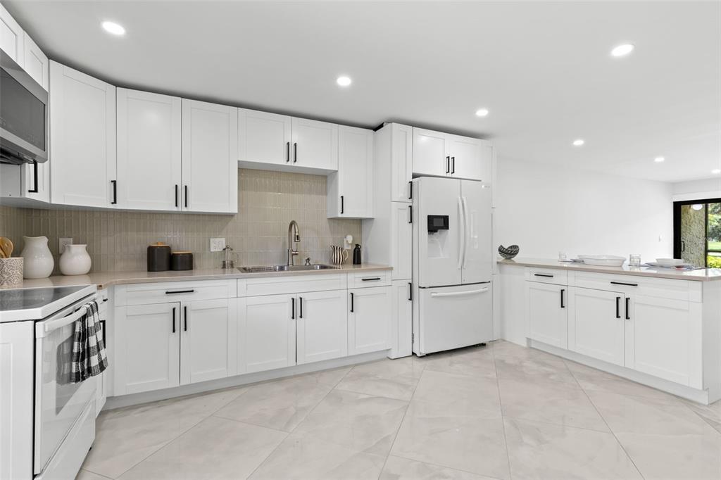 A modern kitchen features white cabinetry, light countertops, a tiled backsplash, and large floor tiles — 2614 COVE CAY DRIVE UNIT 106, CLEARWATER, FL