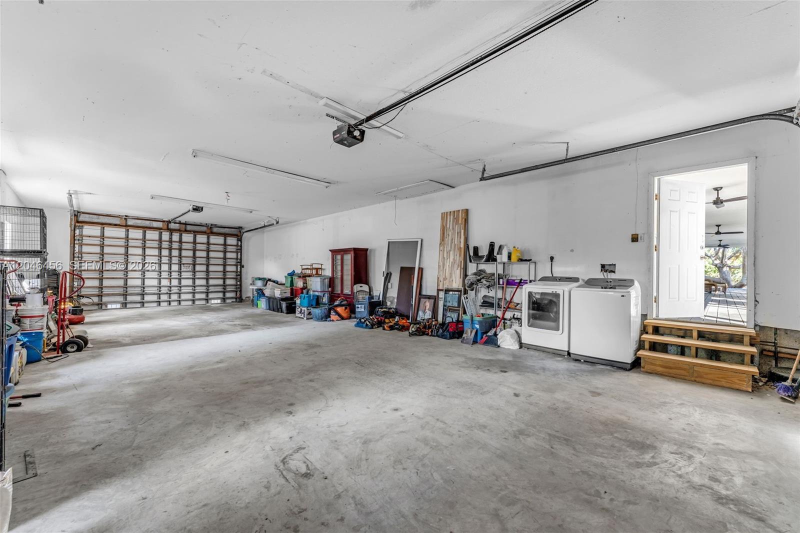A spacious garage with a concrete floor, laundry appliances, and an open exterior door — 20076 SW 190th St, Miami FL 33187, MIAMI, FL