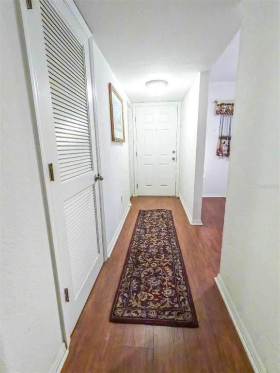 A hallway with wood-look flooring, a louvered closet door, and a patterned runner rug — 175 KINGS HIGHWAY UNIT B5, PUNTA GORDA, FL