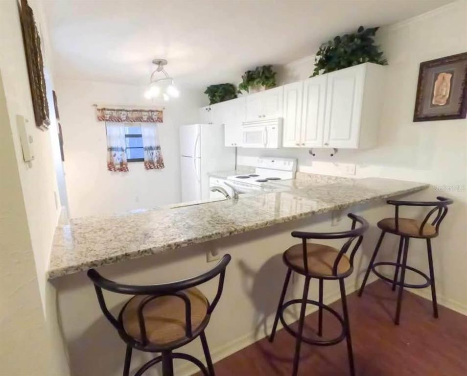 A kitchen features white cabinets, granite countertops, a breakfast bar, and three wooden stools — 175 KINGS HIGHWAY UNIT B5, PUNTA GORDA, FL