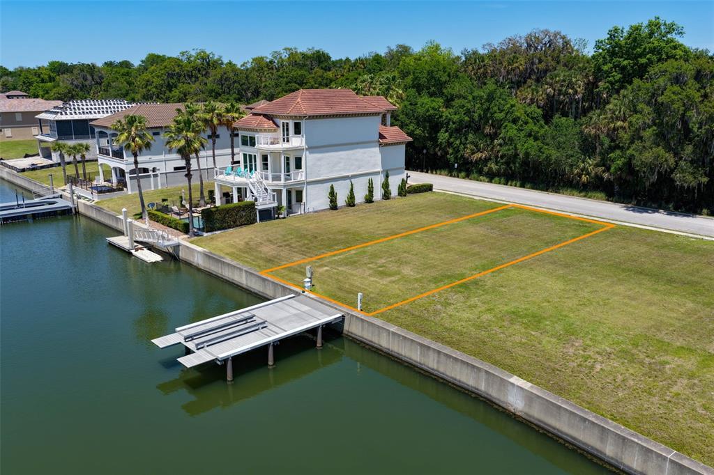 An aerial view shows a vacant waterfront lot outlined in orange next to a house — 216 HARBOR VILLAGE POINT N, PALM COAST, FL