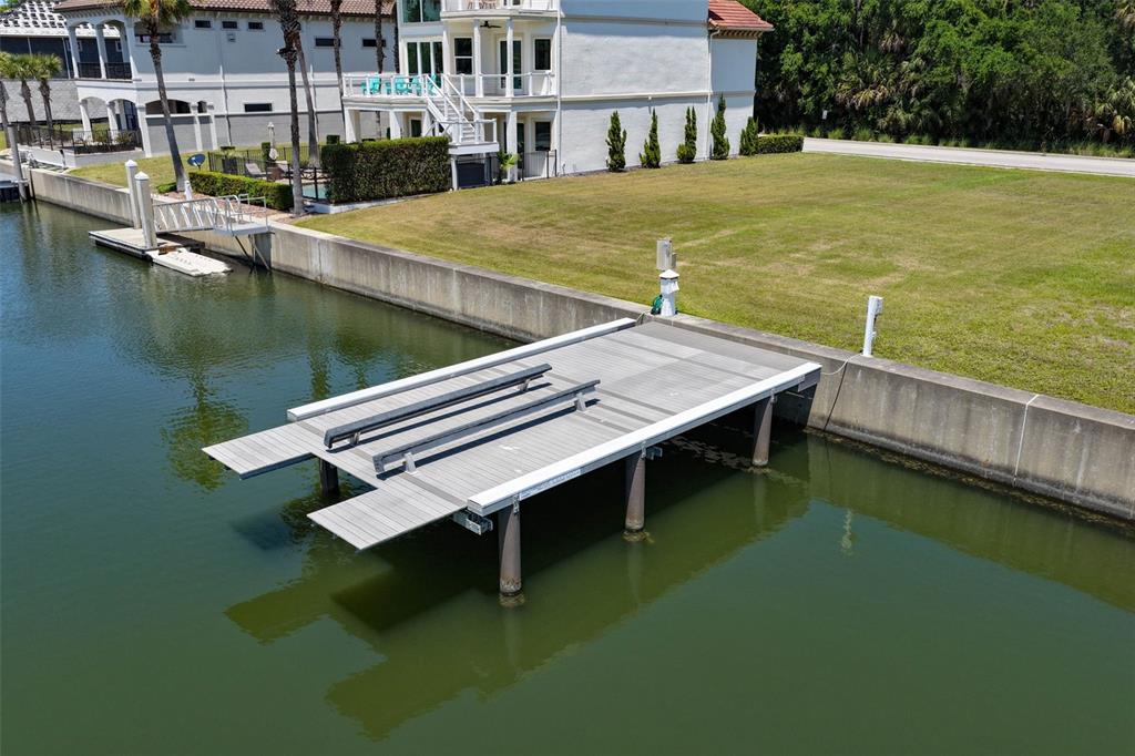 An aerial view shows a boat lift dock extending from a concrete seawall into a canal — 216 HARBOR VILLAGE POINT N, PALM COAST, FL