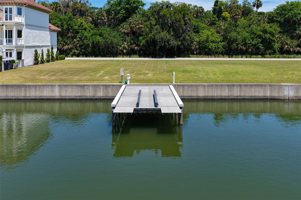 A boat dock extends from a concrete seawall into a canal beside a grassy lot — 216 HARBOR VILLAGE POINT N, PALM COAST, FL