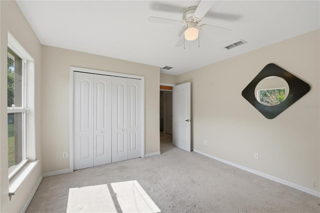 A bedroom with beige walls, carpeted flooring, a ceiling fan, and a diamond-shaped wall mirror — 3119 KEYSTONE POINTE COURT, ST CLOUD, FL