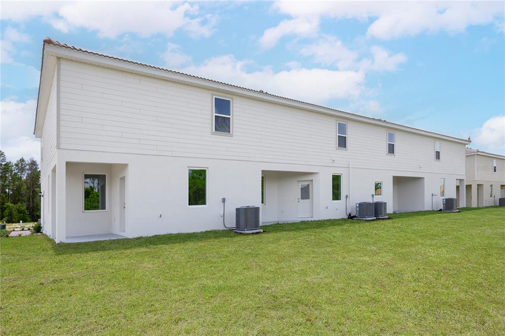 The rear exterior of a two-story townhouse features white siding, stucco, and multiple air-conditioning units — 575 BAY LEAF DRIVE, POINCIANA, FL