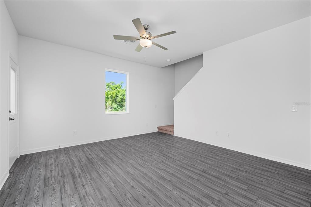 An empty room features gray wood-look flooring, white walls, a ceiling fan, and a window — 575 BAY LEAF DRIVE, POINCIANA, FL