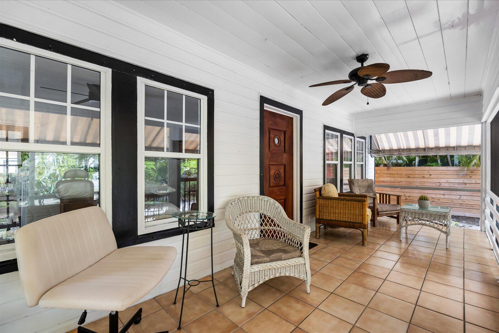 A covered porch features white wood walls, black window frames, tiled flooring, and outdoor furniture — 705 SE Stypmann Boulevard, Stuart FL 34994, STUART, FL