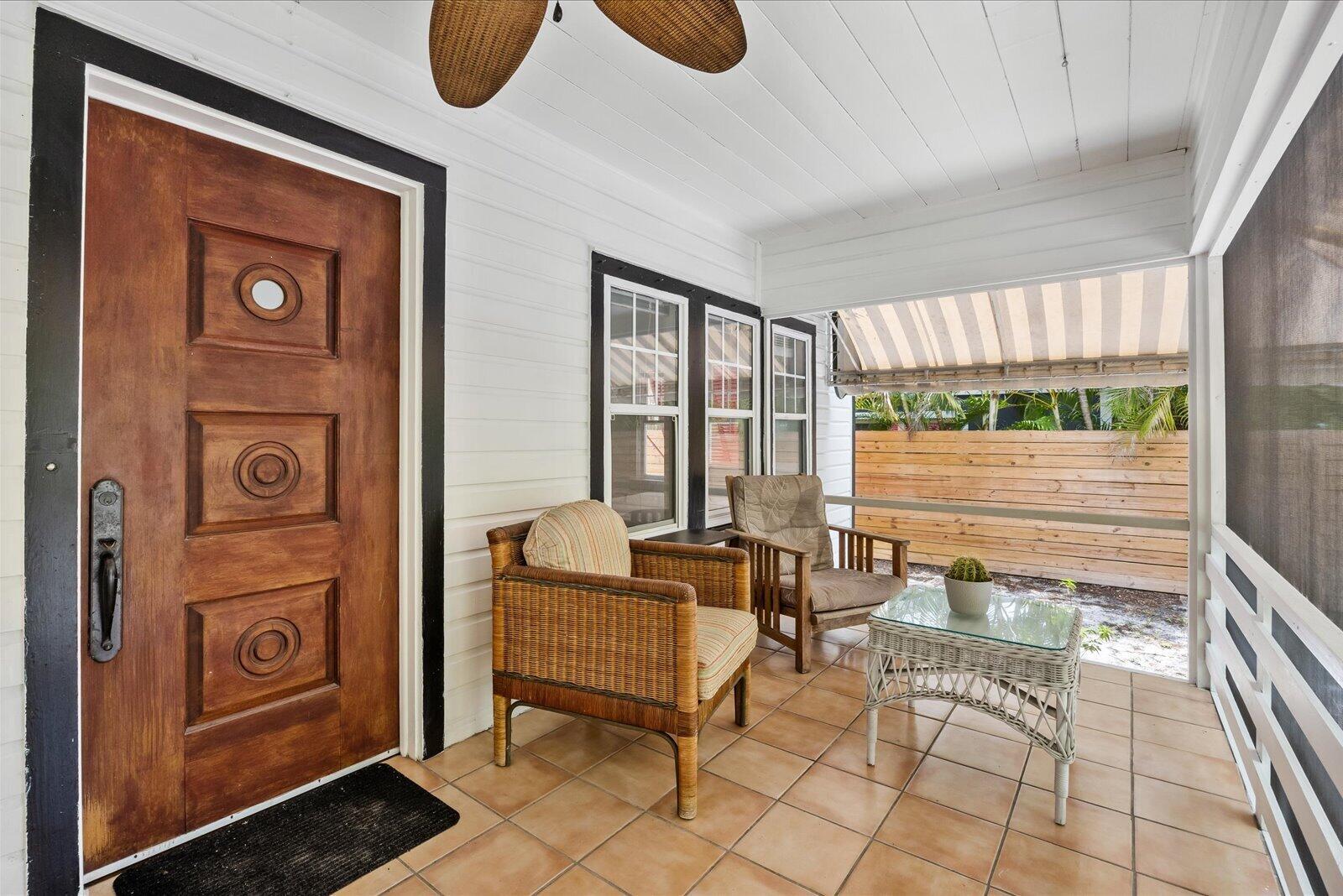 A covered porch features a wooden door, wicker chairs, a glass-topped table, and tiled flooring — 705 SE Stypmann Boulevard, Stuart FL 34994, STUART, FL