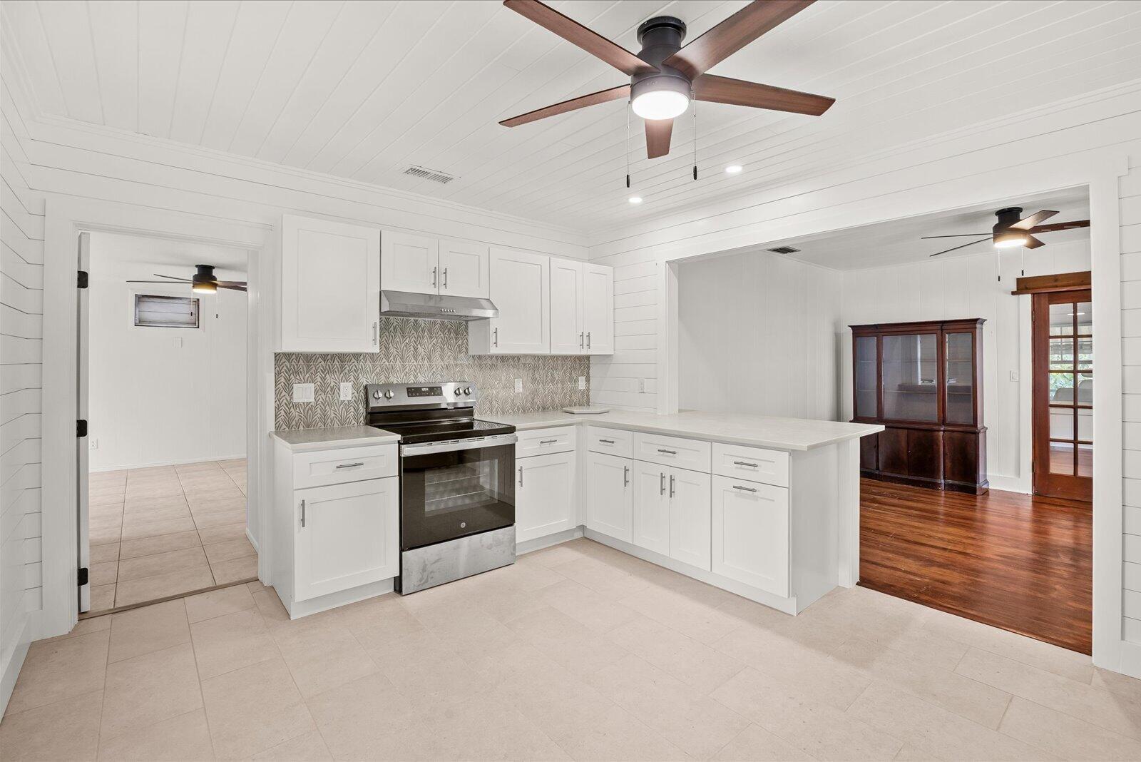 A white kitchen features shaker cabinets, a patterned backsplash, and a peninsula with stone countertops — 705 SE Stypmann Boulevard, Stuart FL 34994, STUART, FL