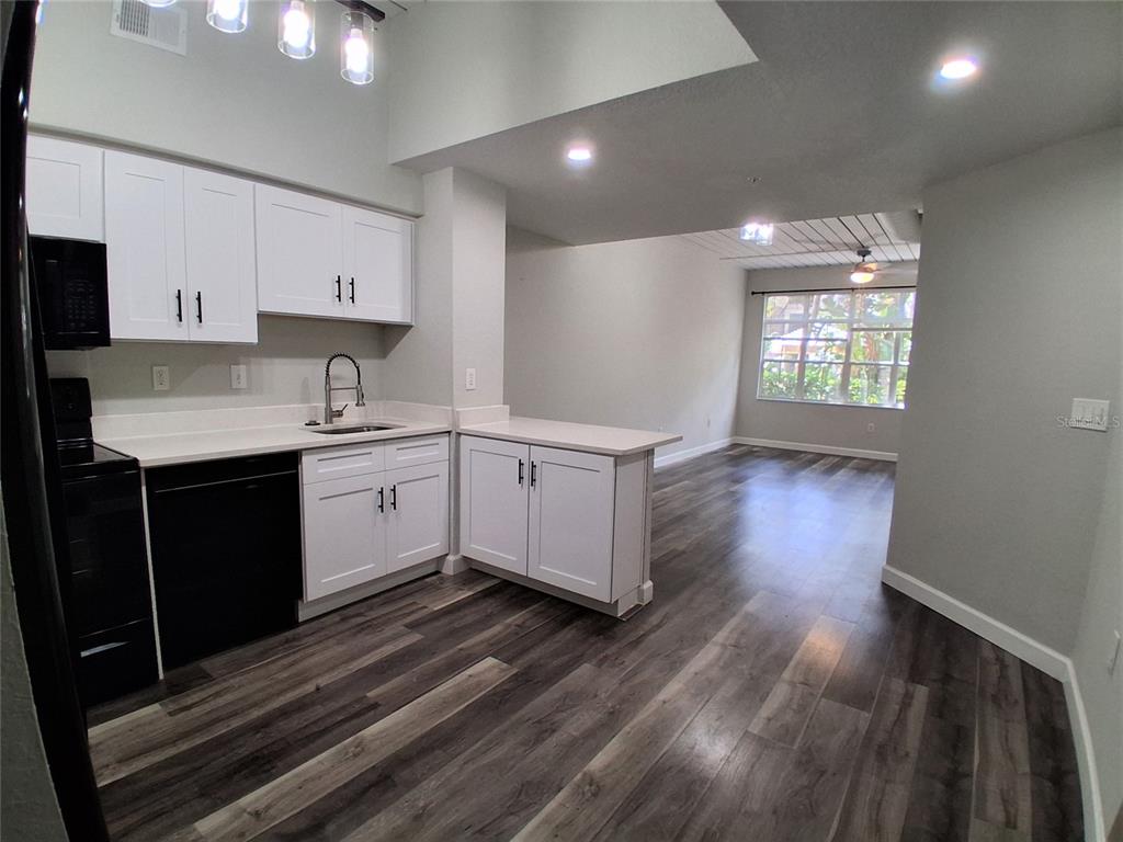 A kitchen with white cabinets and dark appliances opens into a living area with wood-look flooring — 2402 W AZEELE STREET UNIT 417, TAMPA, FL
