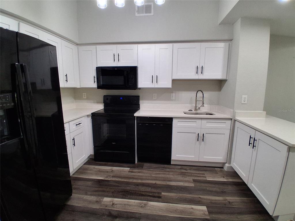 A kitchen features white cabinets, black appliances, a light countertop, and wood-look flooring — 2402 W AZEELE STREET UNIT 417, TAMPA, FL