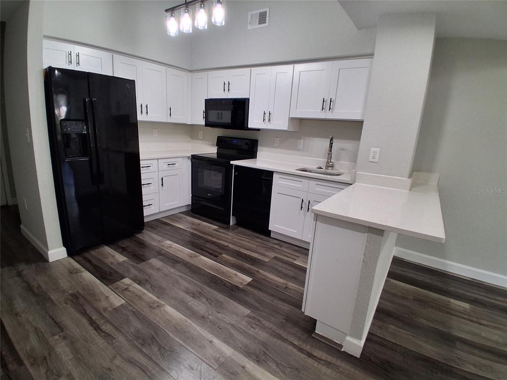A kitchen features white cabinets, black appliances, quartz countertops, and wood-look flooring — 2402 W AZEELE STREET UNIT 417, TAMPA, FL