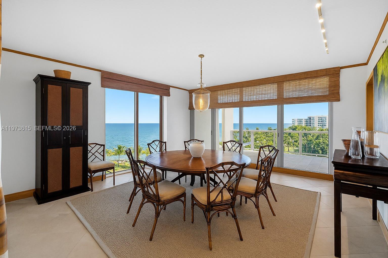 A dining room features a round wooden table, rattan chairs, and floor-to-ceiling ocean views — 430 Grand Bay Dr # 801, Key Biscayne FL 33149, KEY BISCAYNE, FL