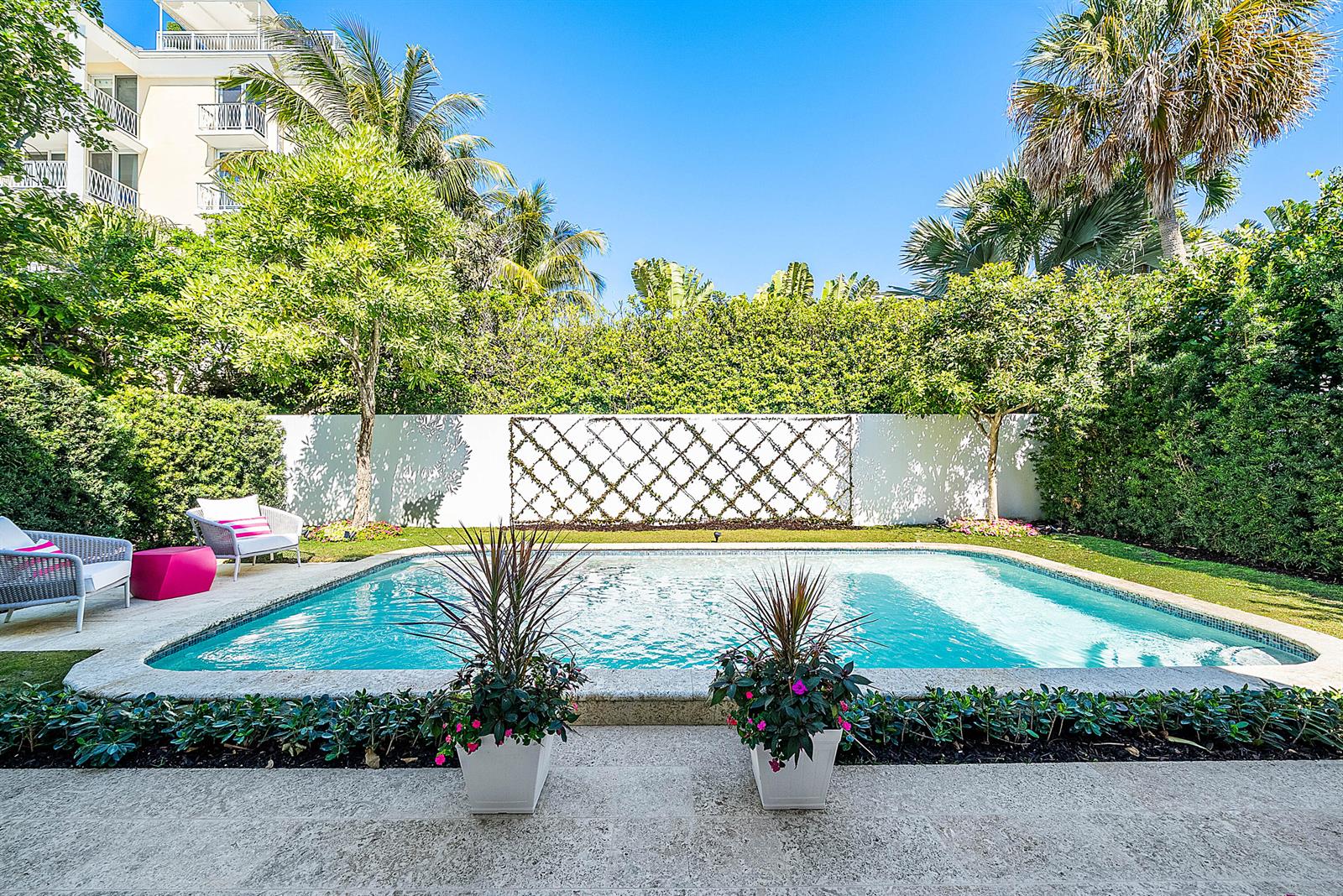 A rectangular swimming pool sits in a backyard with a white wall and lattice trellis — 157 Peruvian Avenue, Palm Beach FL 33480, PALM BEACH, FL