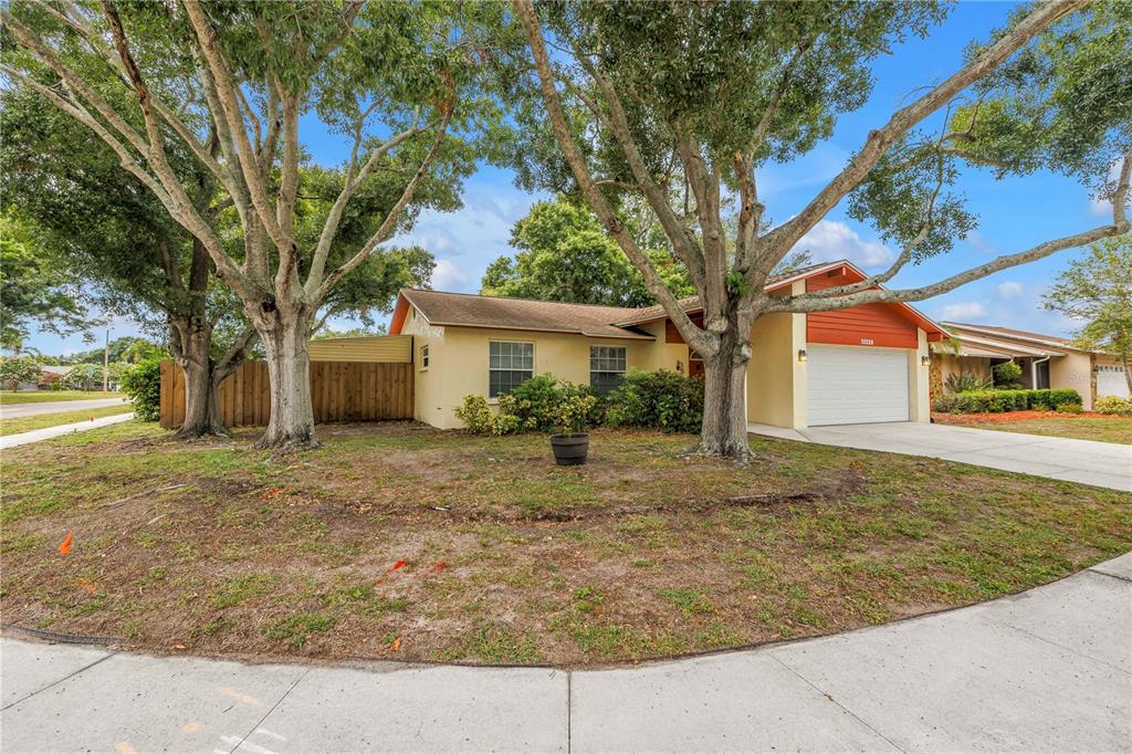A single-story house with a white garage, tan exterior, and large trees in the front yard — 12220 WILD ACRES ROAD, LARGO, FL