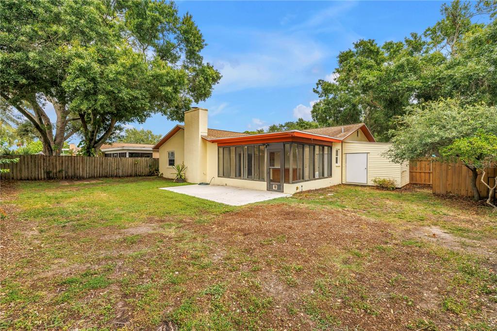 A backyard view of a house with a screened-in porch, concrete patio, and wooden fence — 12220 WILD ACRES ROAD, LARGO, FL
