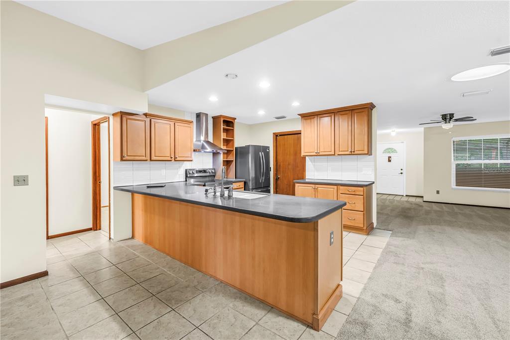 A kitchen with wood cabinets, dark countertops, and tile flooring opens into a carpeted living area — 12220 WILD ACRES ROAD, LARGO, FL