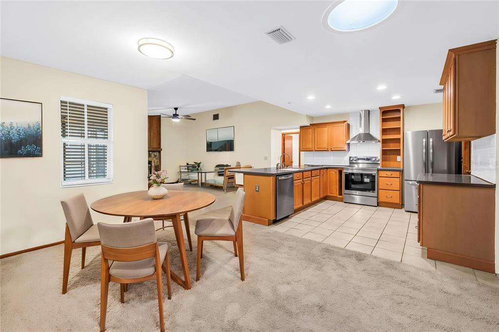 An open-concept kitchen and dining area with wood cabinets, stainless appliances, and carpeted flooring — 12220 WILD ACRES ROAD, LARGO, FL