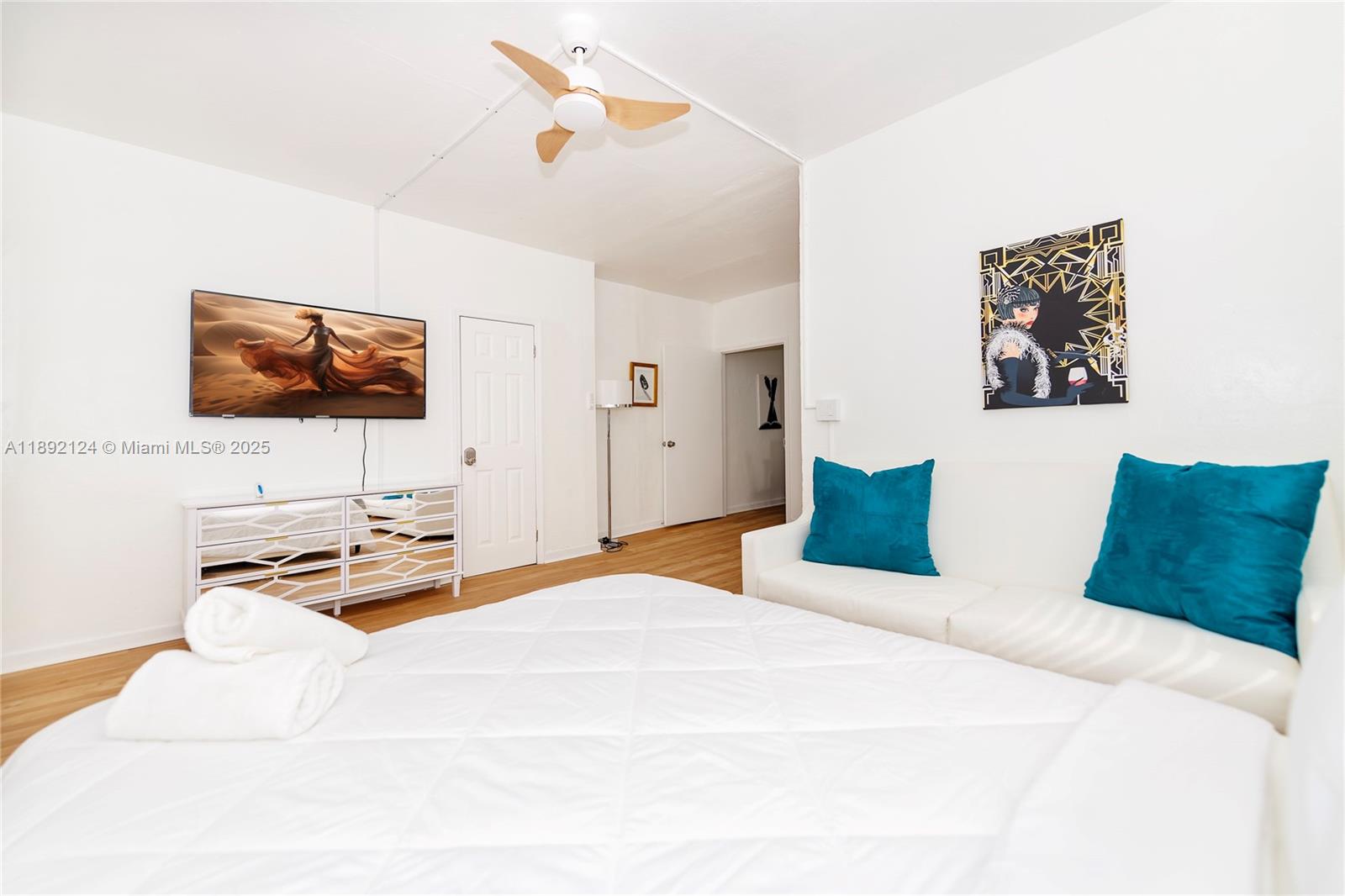 A bedroom features a white bed, a mirrored dresser, a television, and teal accent pillows — 545 Michigan Ave # 2, Miami Beach FL 33139, MIAMI BEACH, FL