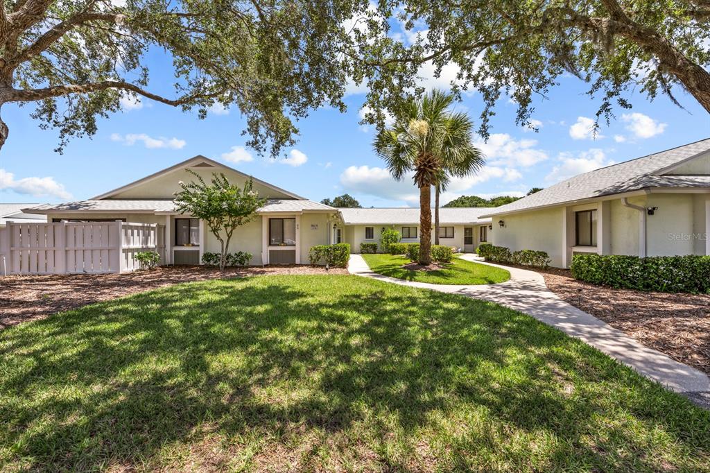 A view of a single-story residential building exterior with a lawn, palm tree, and walkway — 39 LAKE FOREST PLACE, PALM COAST, FL