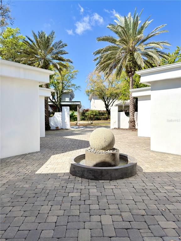 A stone sphere fountain sits in the center of a paved courtyard between white buildings — 6049 LADY BET DRIVE, ORLANDO, FL