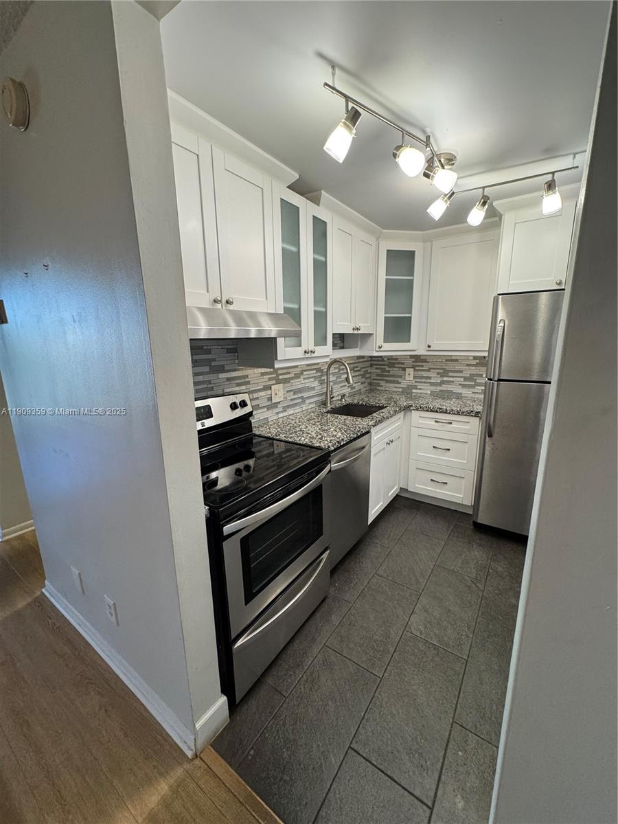 A galley kitchen features white cabinets, stainless steel appliances, granite countertops, and gray tile flooring — 8411 NW 8th St # 203, Miami FL 33126, MIAMI, FL