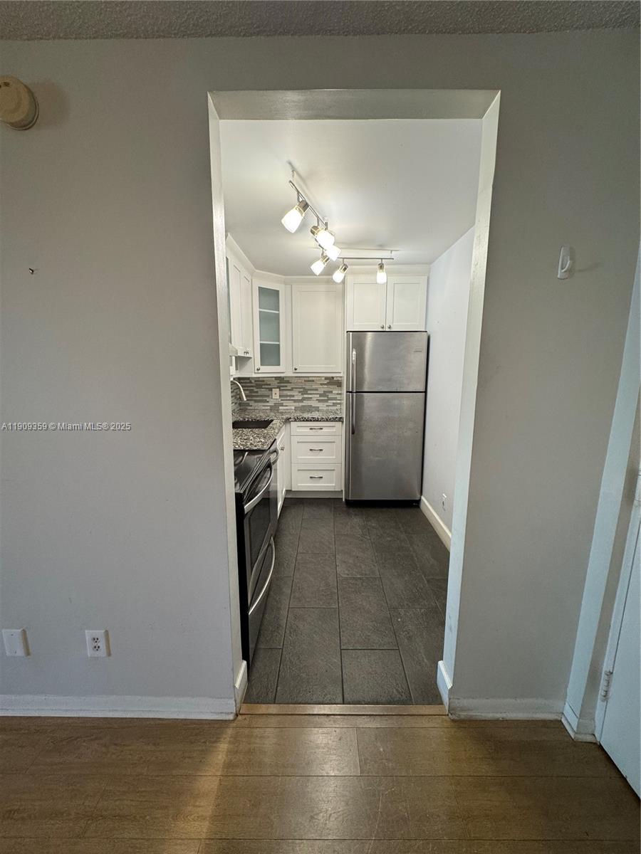A galley kitchen features white cabinets, stainless steel appliances, and dark tile flooring — 8411 NW 8th St # 203, Miami FL 33126, MIAMI, FL