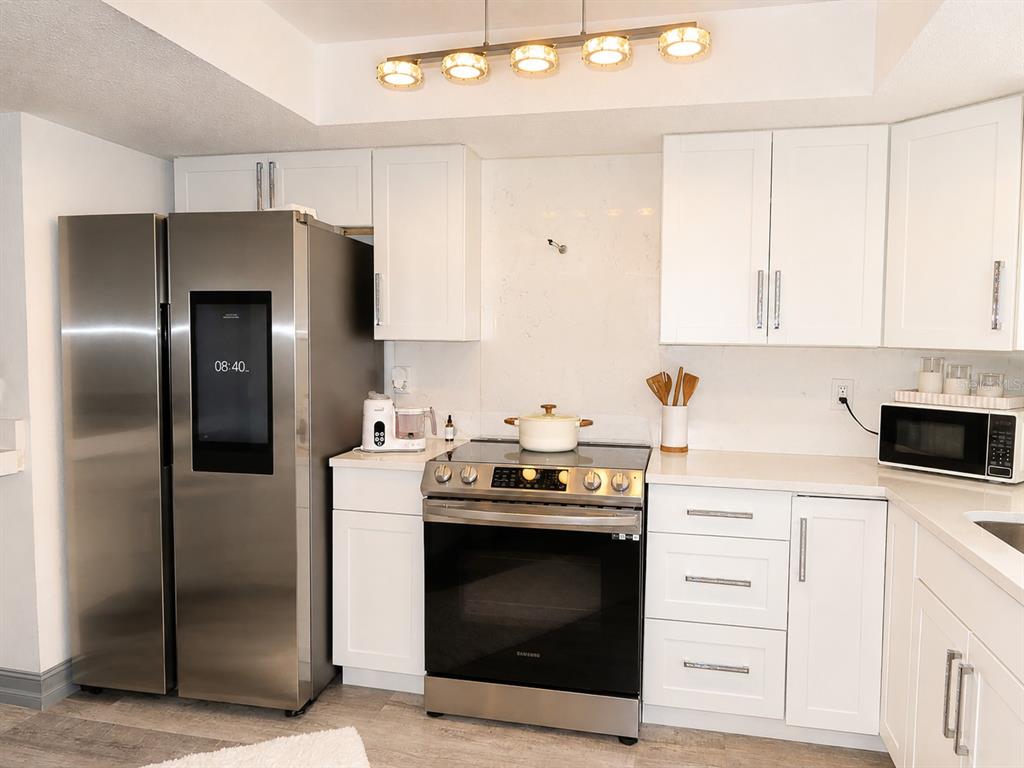 A kitchen features white cabinets, stainless steel appliances, a smart refrigerator, and a light-colored backsplash — 6301 58TH STREET N UNIT 402, PINELLAS PARK, FL