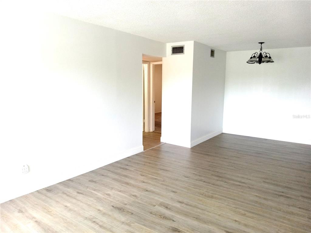 An empty room with light wood-look flooring, white walls, and a hanging chandelier — 2359 FINLANDIA LANE UNIT 65, CLEARWATER, FL