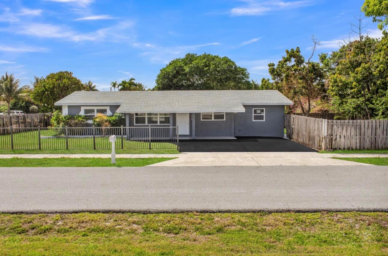 A single-story gray house with a white door, asphalt driveway, and a fenced front yard — 915 SW 3rd Street, Boynton Beach FL 33435, BOYNTON BEACH, FL