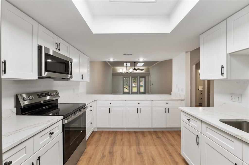 A modern kitchen features white cabinets, stainless steel appliances, and light wood-look flooring — 6245 NW 106TH PLACE, ALACHUA, FL