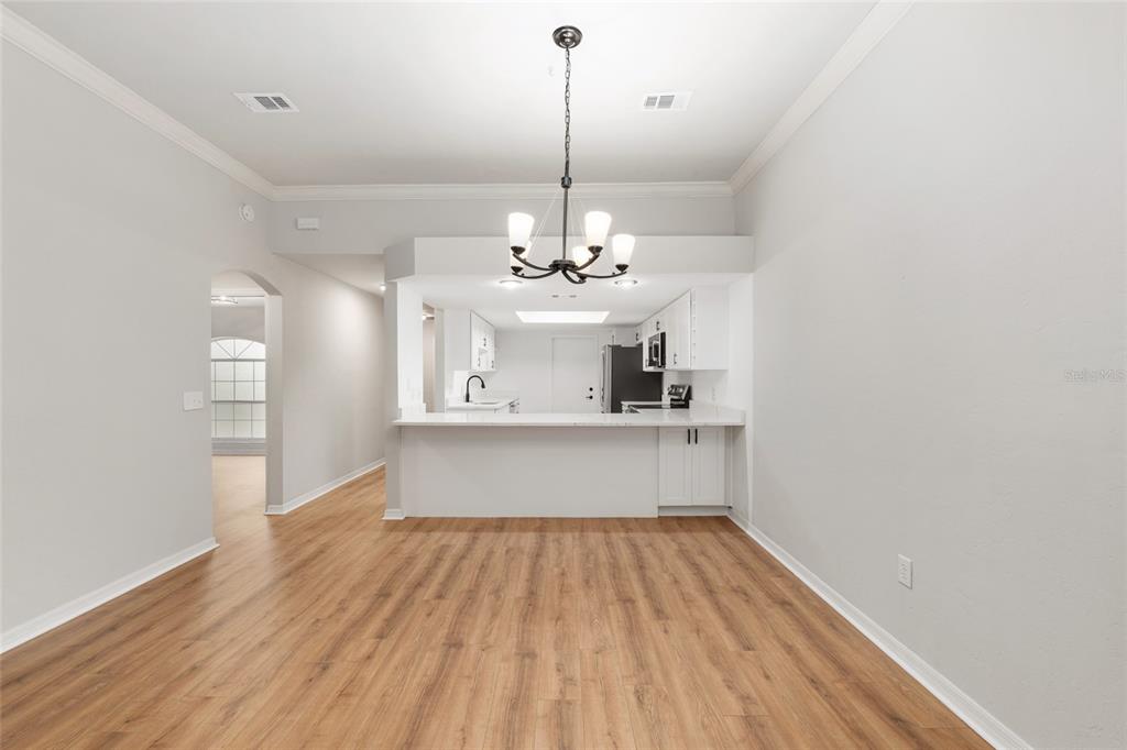 A kitchen features white cabinets, a marble-look countertop, a breakfast bar with three stools, and stainless appliances — 6245 NW 106TH PLACE, ALACHUA, FL