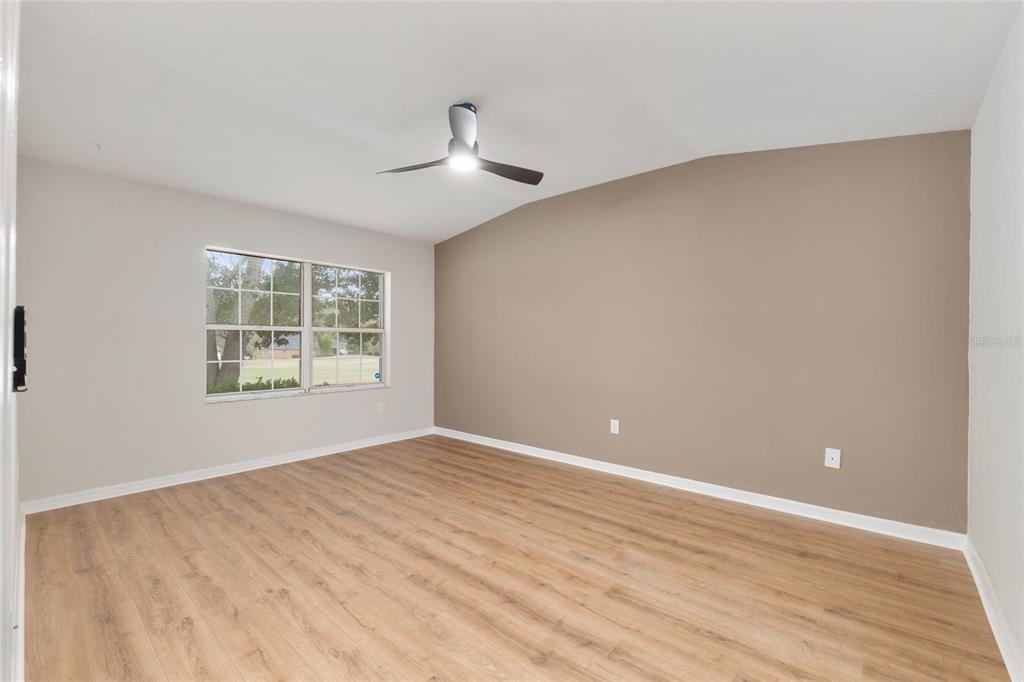 An empty bedroom features light wood-look flooring, a ceiling fan, and a tan accent wall — 6245 NW 106TH PLACE, ALACHUA, FL