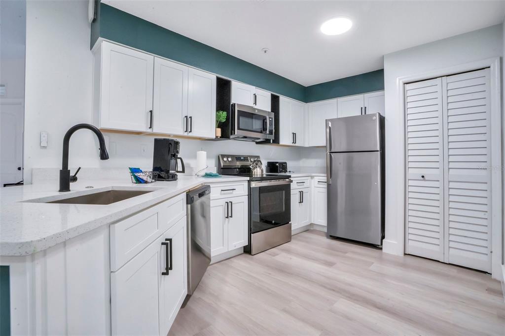 A kitchen features white cabinets, stainless steel appliances, quartz countertops, and a teal accent wall — 8763 WORLDQUEST BOULEVARD UNIT 5105, ORLANDO, FL