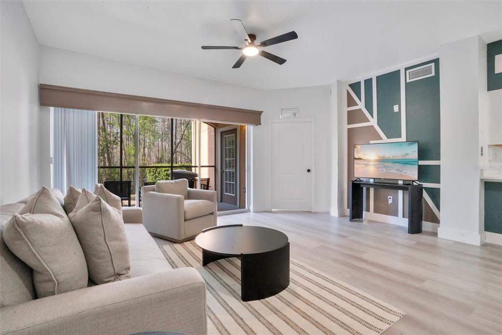 A living room features light wood flooring, a patterned accent wall, and a sliding glass door — 8763 WORLDQUEST BOULEVARD UNIT 5105, ORLANDO, FL