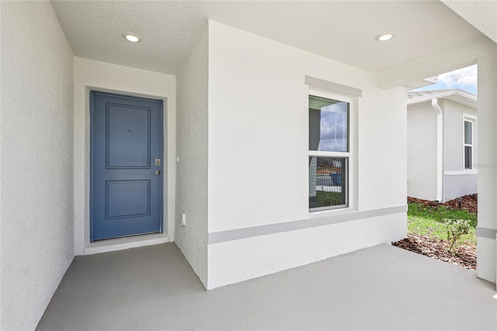 A covered front porch features a blue door, a single window, and recessed lighting — 1111 AMBER WAVES COURT, LAKE WALES, FL