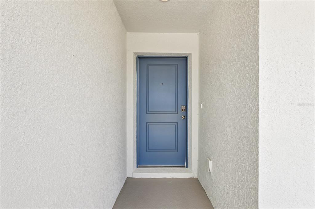A blue front door is set within a recessed entryway with white stucco walls — 1111 AMBER WAVES COURT, LAKE WALES, FL