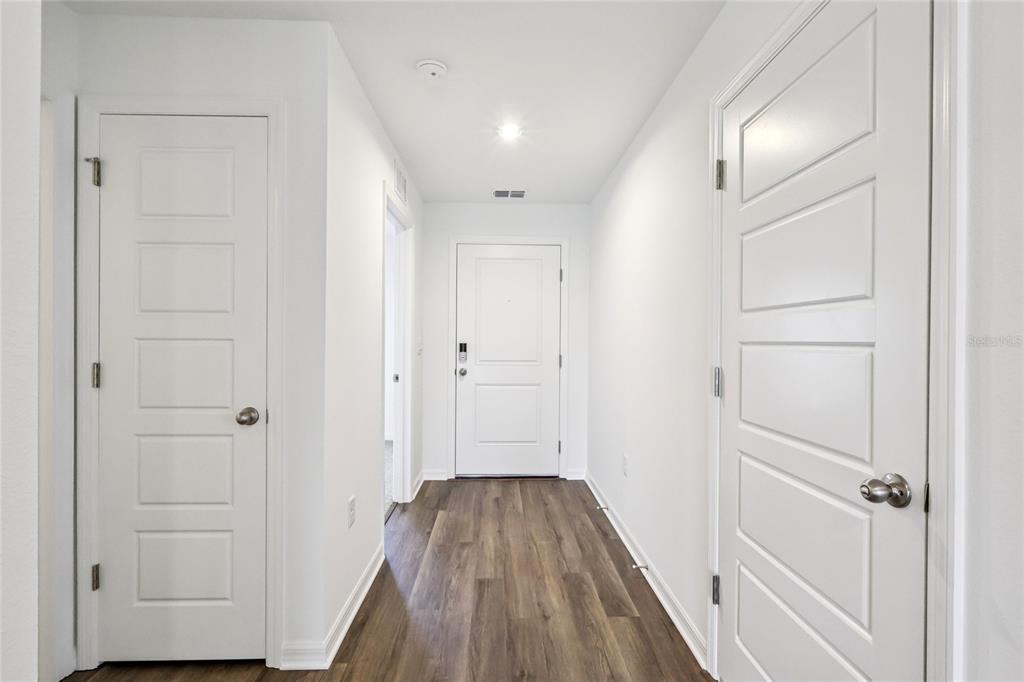 A hallway with wood-look flooring leads to a white front door between two interior doors — 1111 AMBER WAVES COURT, LAKE WALES, FL