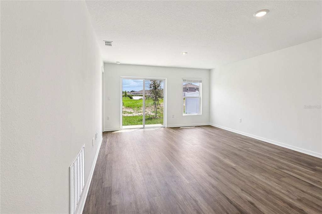 An empty living room features wood-look flooring, white walls, recessed lighting, and a sliding glass door — 1111 AMBER WAVES COURT, LAKE WALES, FL