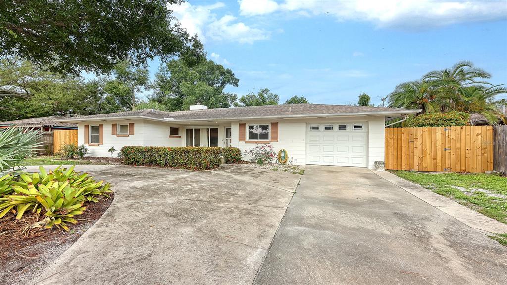 A single-story house with a white exterior, a concrete driveway, and a wooden privacy fence — 4735 REMINGTON DRIVE, SARASOTA, FL