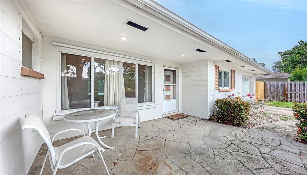 A white house exterior features a stone patio, a large window, and a glass door — 4735 REMINGTON DRIVE, SARASOTA, FL