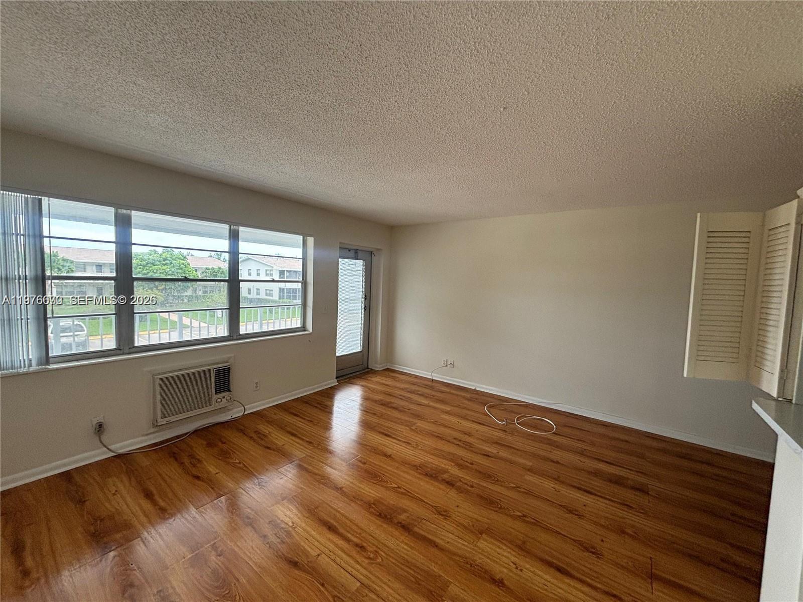 An empty room features wood-look flooring, a window air conditioning unit, and a glass door — 36 Windsor # B, West Palm Beach FL 33417, WEST PALM BEACH, FL