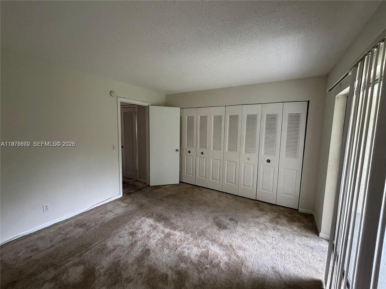 An empty bedroom features beige carpeting, white walls, and a wall of louvered closet doors — 36 Windsor # B, West Palm Beach FL 33417, WEST PALM BEACH, FL